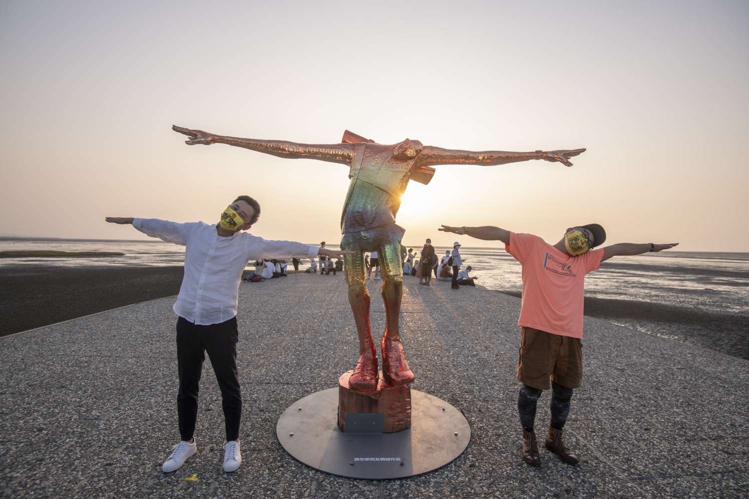 新竹市長林智堅與日本藝術家阿部乳坊在賞蟹步道與七彩「旅人」一同張開雙臂，歪頭看夕陽。